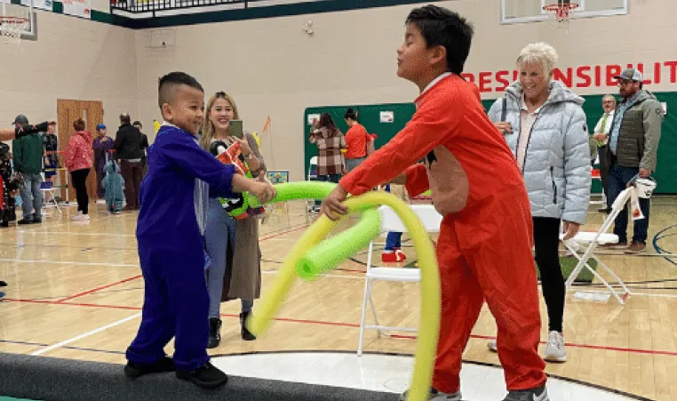 Two children play with noodles on the balance beam while their families look on at the Sturgeon Bay Halloween party.