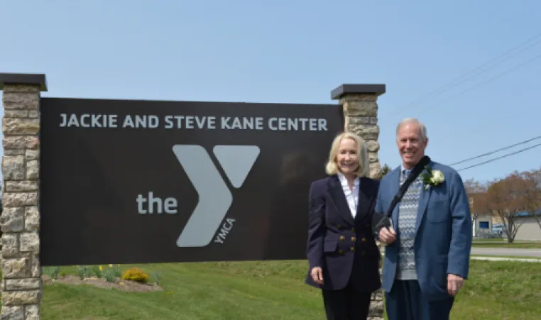 Jackie and Steve Kane pose outside next to the new exterior sign with the text "Jackie and Steve Kane Center"