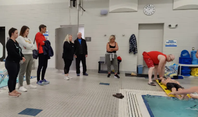 Staff members look on as a water rescue is performed by a pool.