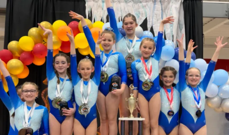 A group of Strivers gymnasts pose on the podium with their medals and trophy.